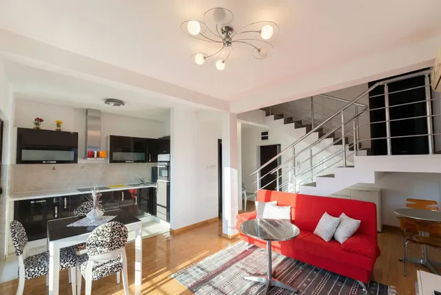 Современная кухня-гостиная с красным диваном и лестницей в квартире в Бечичи, Черногория.