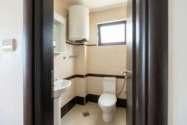 Современный санузел с бойлером, раковиной и окном в квартире в Бечичи, Черногория. Светлая плитка, качественная отделка.