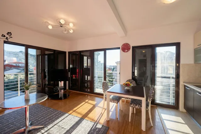 Светлая гостиная с обеденной зоной и панорамными окнами в квартире в Бечичи, Черногория, с видом на горы и море.