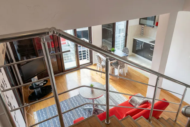 Вид сверху на гостиную с красным диваном и кухней в квартире в Бечичи, Черногория. Современный интерьер с лестницей.