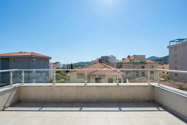 Просторная терраса с видом на море и город в апартаментах Бечичи, Черногория, с современным стеклянным ограждением.