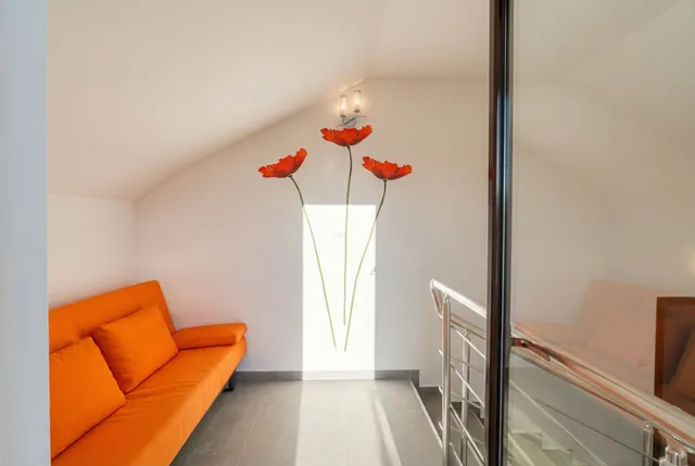 Зона отдыха с оранжевым диваном и декором в виде маков в квартире в Бечичи, Черногория. Мансардный этаж с лестницей.